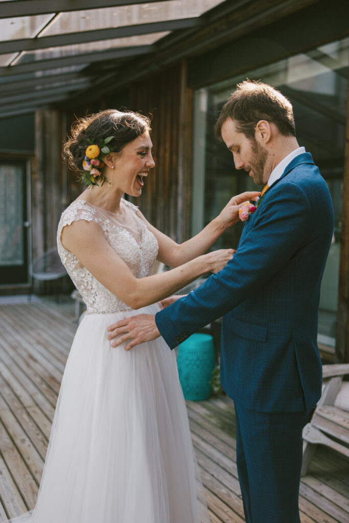 A documentary style wedding photo of a bride who has a big smile on her face as she points to the groom's boutonniere.