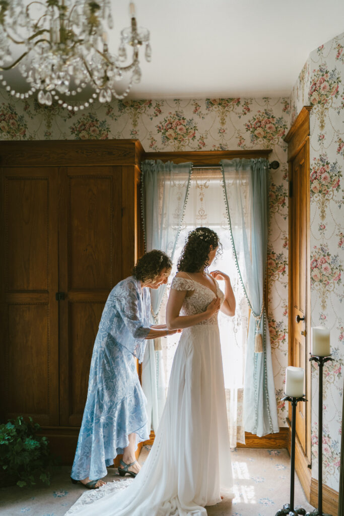 A bride standing in front of a window in a vintage looking room taken by a documentary style wedding photographer