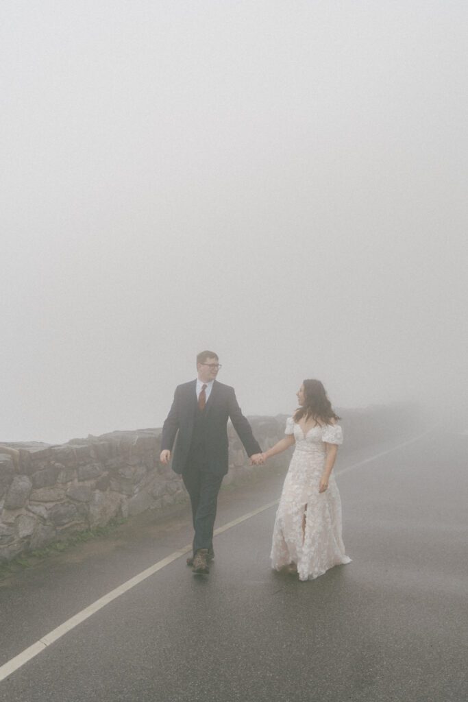 Bride and groom hold hands and walk through fog during their spring elopement in Colorado.
