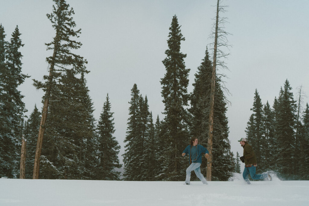 Couple runs through deep snow during a winter engagement session in Colorado.